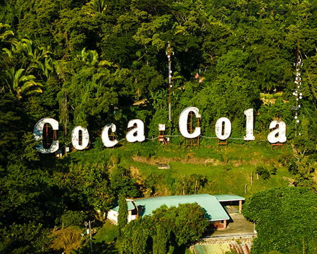 Paisaje de un bosque visto desde el aire con un cartel de Coca-Cola blanco.