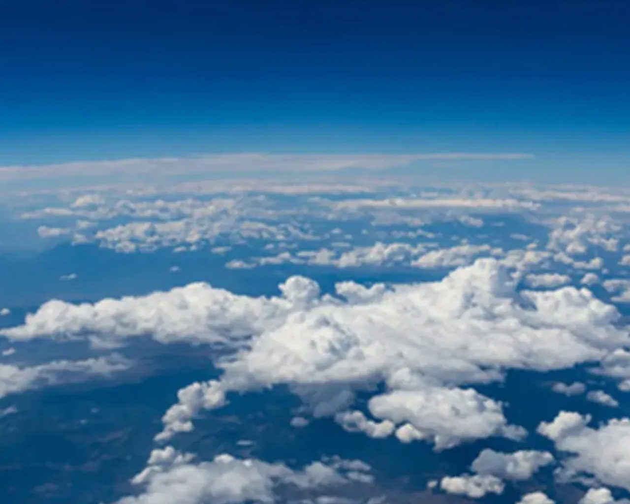 Vista aérea de nubes blancas y esponjosas sobre un paisaje azul, vistas desde la altitud de un avión, con un ligero desenfoque en los bordes.