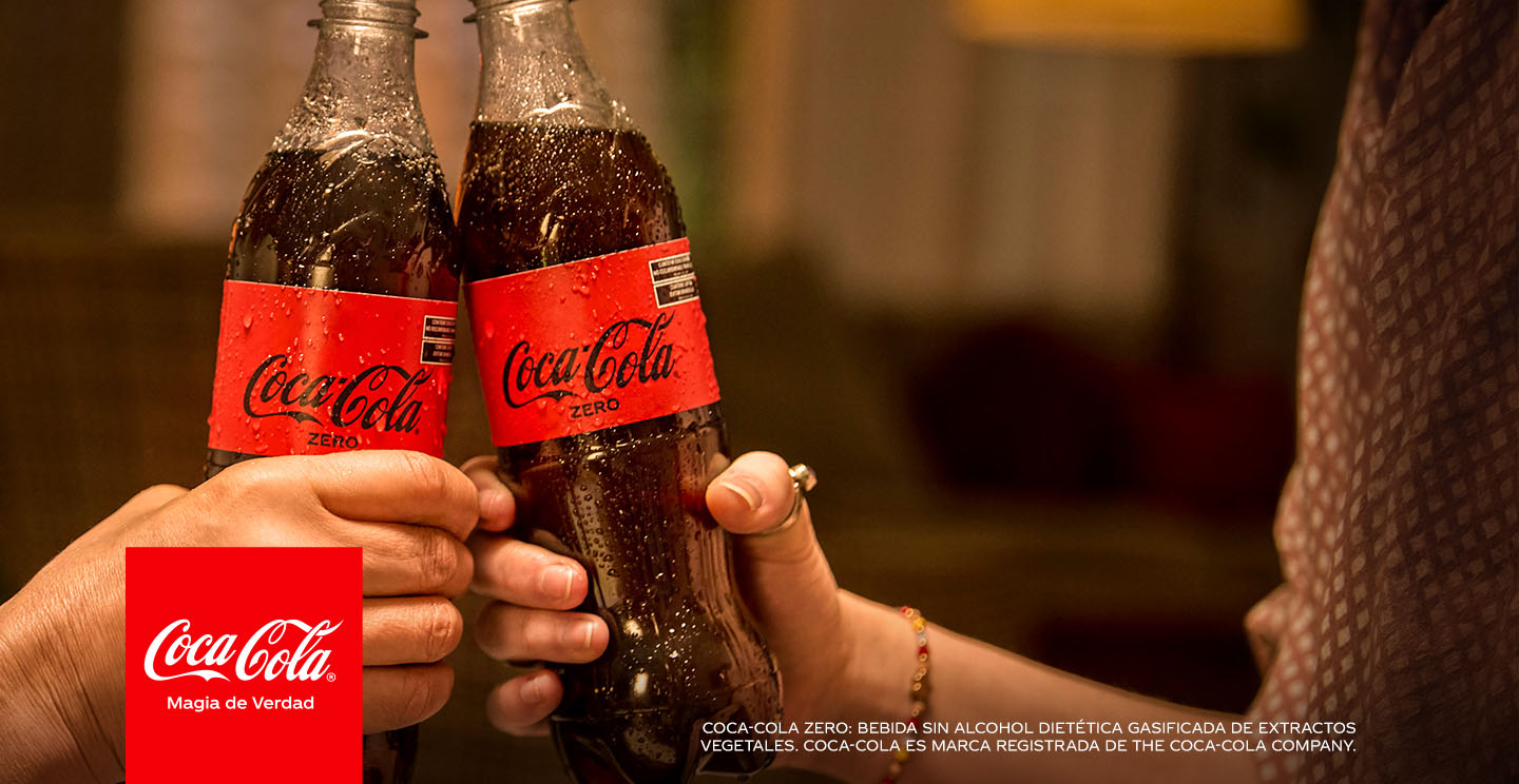 Dos manos sosteniendo y brindando con una Coca-Cola Zero.