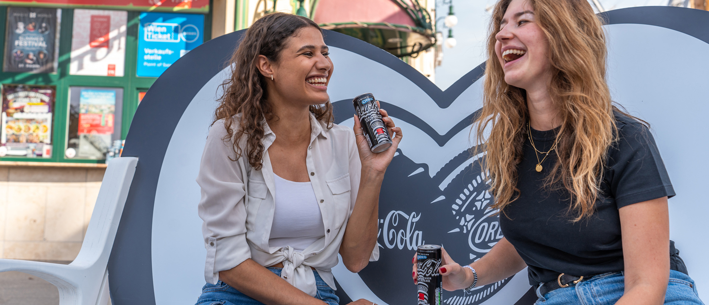 Zwei Personen auf der Bestie-Bank Platz mit dem brandneue Coca-Cola OREO® Zero Sugar