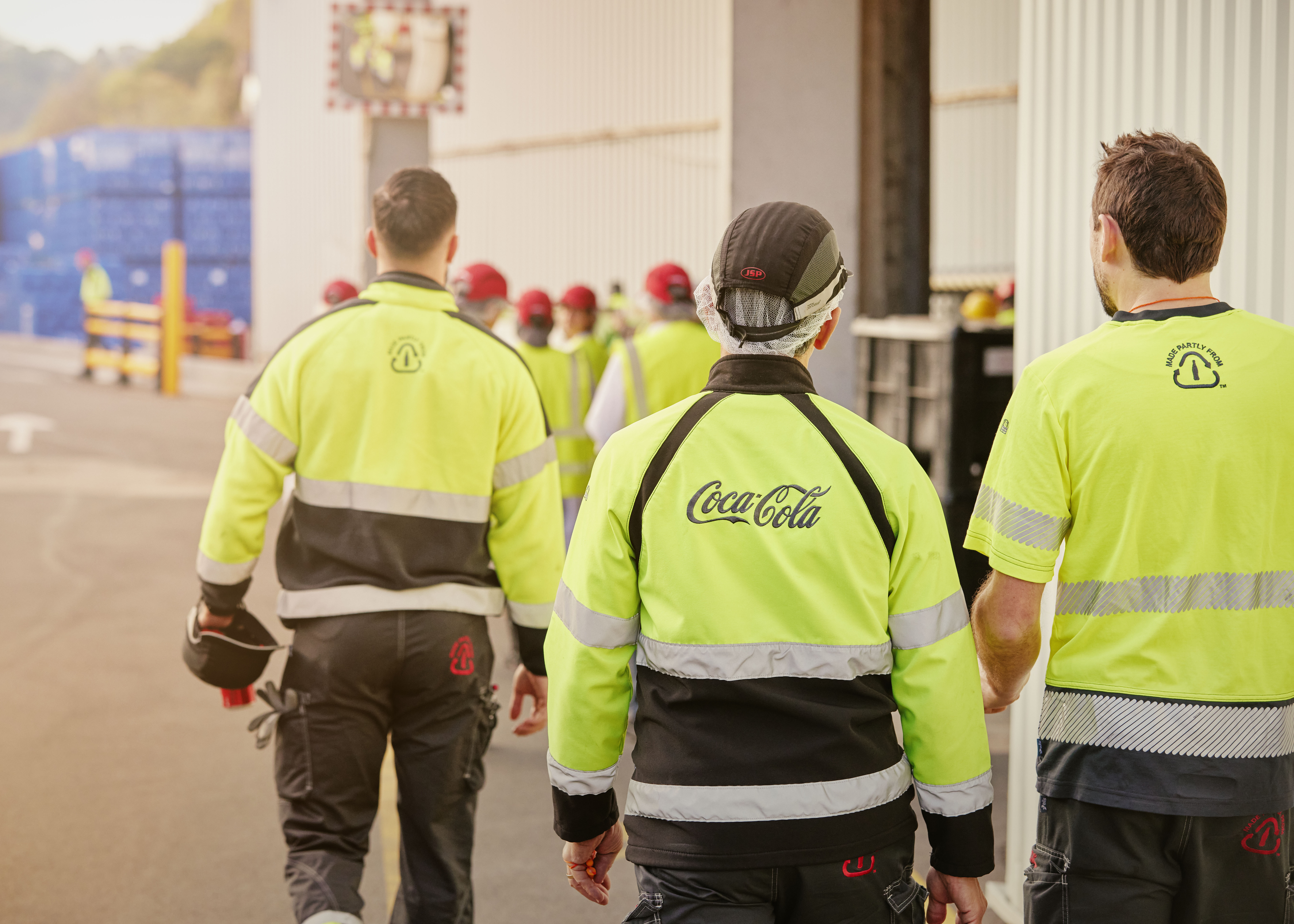 Coca-Cola werknemers wandelen met veiligheidskledij door fabriek