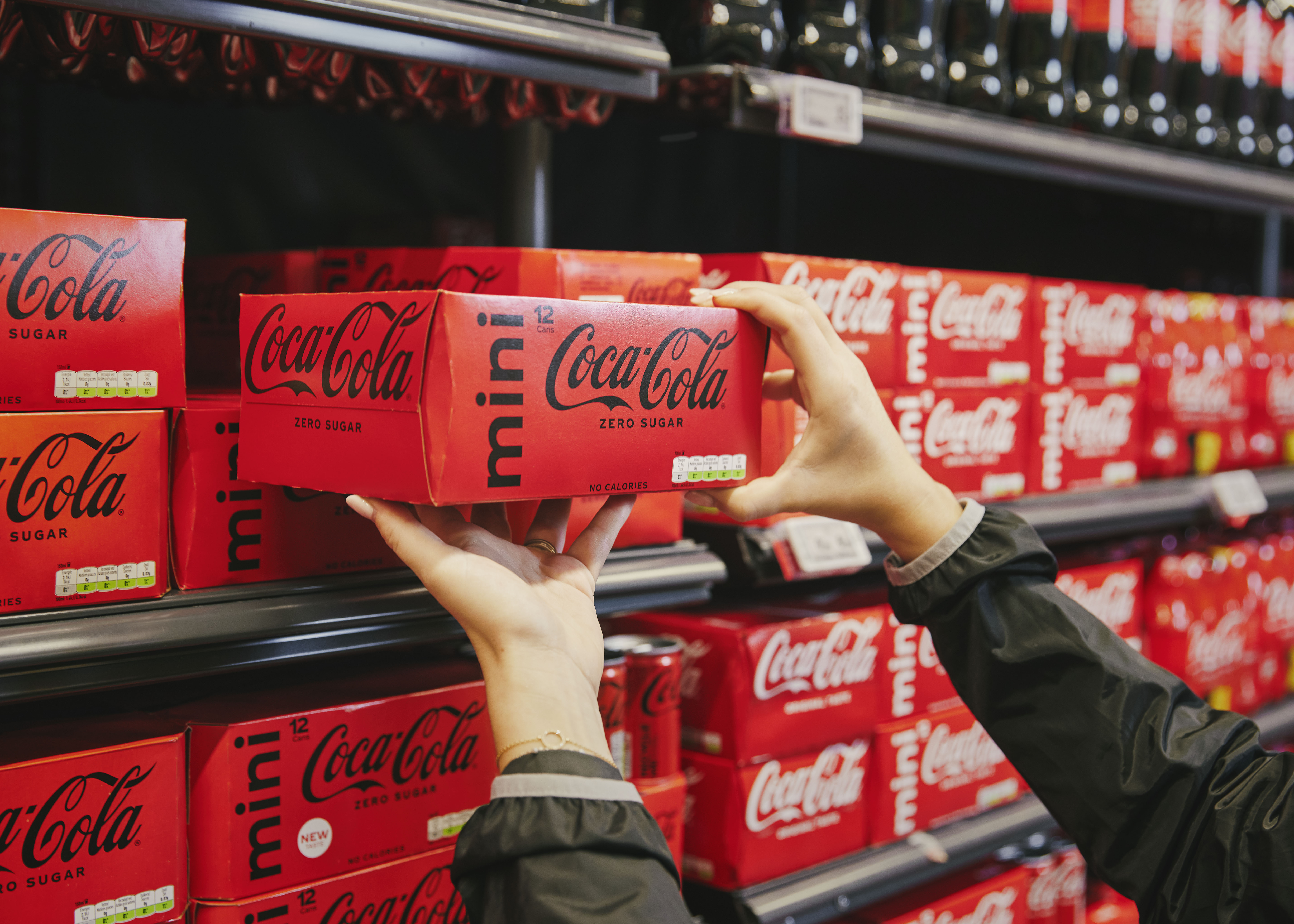 Handen nemen een verpakking Coca-Cola mini uit een winkelrek