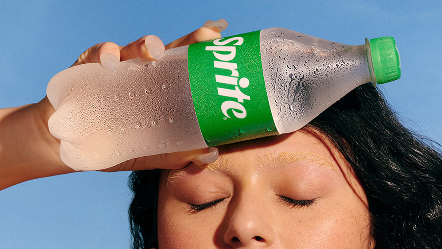 Uma mulher se refresca em um dia quente de verão segurando uma garrafa gelada de Sprite na testa.