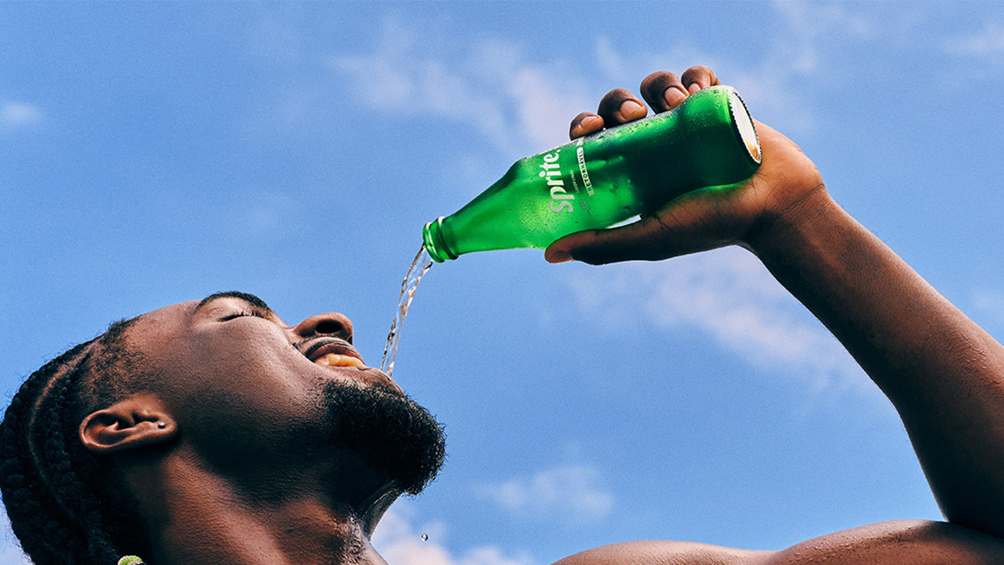 Um homem mata a sede bebendo Sprite gelada direto de uma garrafa de vidro no calor intenso do verão.