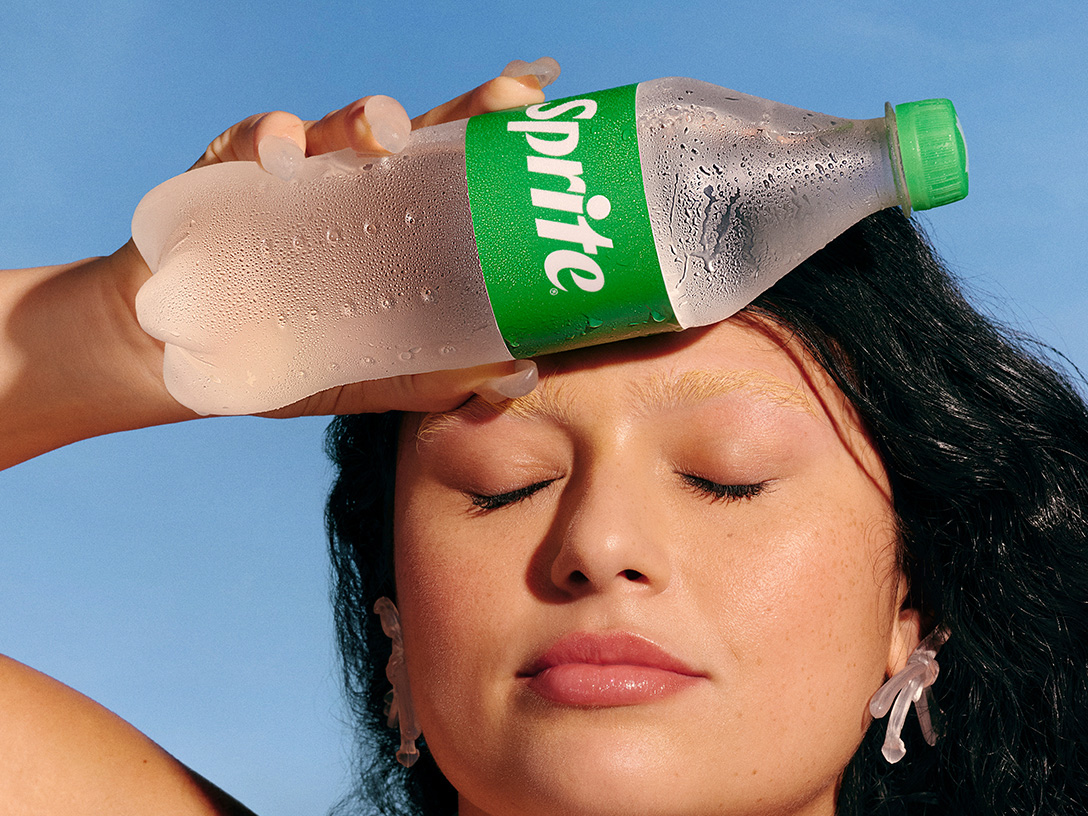 Uma mulher se refresca em um dia quente de verão segurando uma garrafa gelada de Sprite na testa.