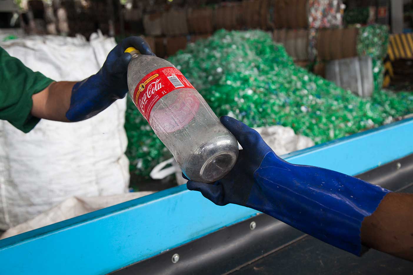 lugar com produtos reciclados. Dois braços com luvas são vistos reciclando uma garrafa retornável de Coca-Cola