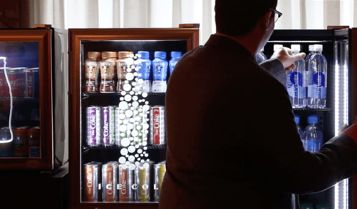 Man standing in front of a fridge grabbing a bottle of water