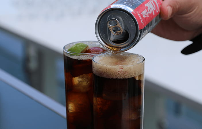 Une main versant du Coke Diète dans un verre 