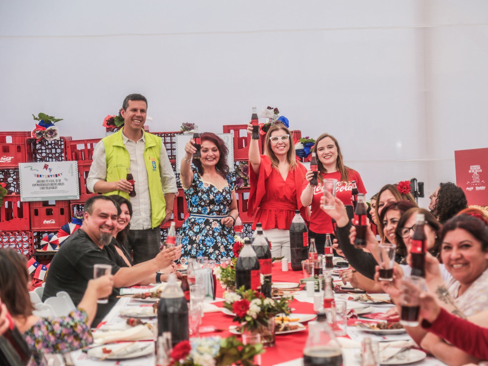 personas sentadas al rededor de una mesa, brindando con una botella PET de Coca-Cola en la mano.