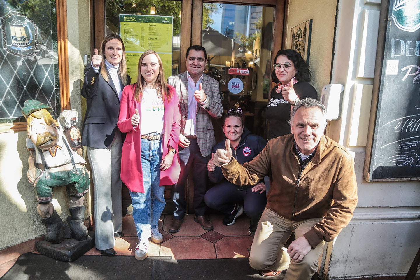 Imagen de personas en la puerta de un restaurante levantando el dedo pulgar