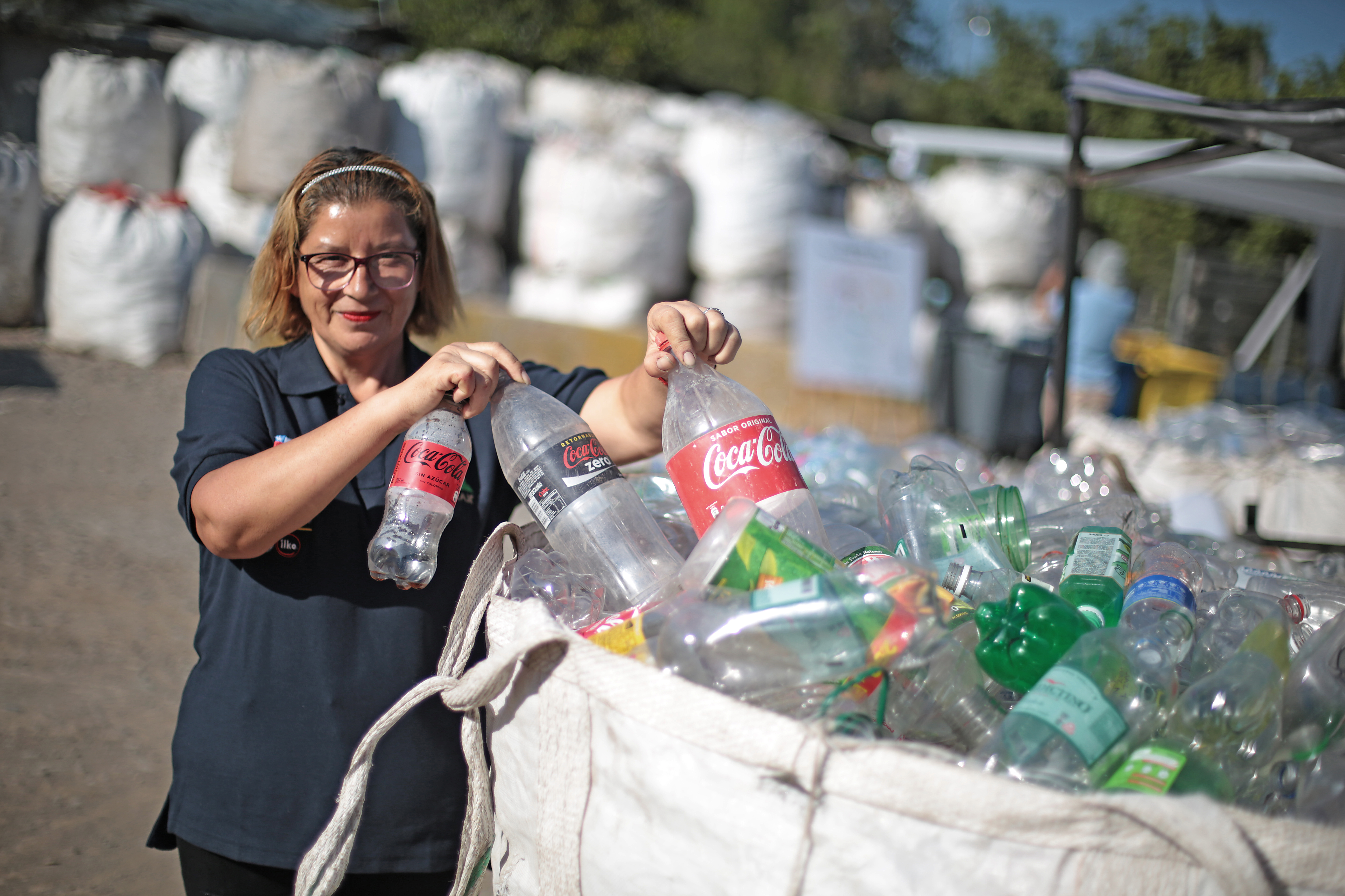 Una recicladora guarda en una bolsa, botellas de plástico de Coca-Cola vacías