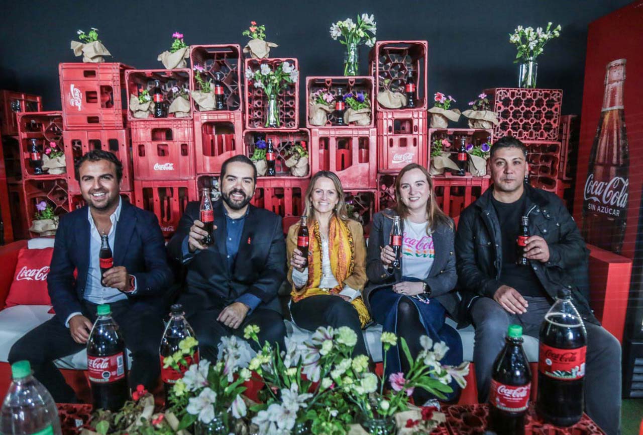 Representantes de Coca-Cola Chile sonrien a la cámara sosteniendo botellas de Coca-Cola