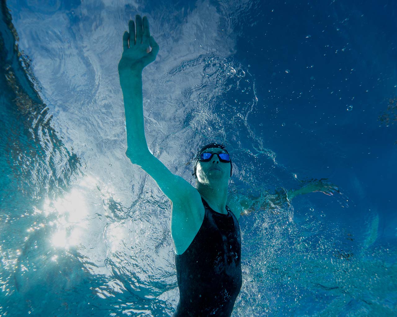 Atleta nadando con una malla negra, antiparras y gorro de natación.