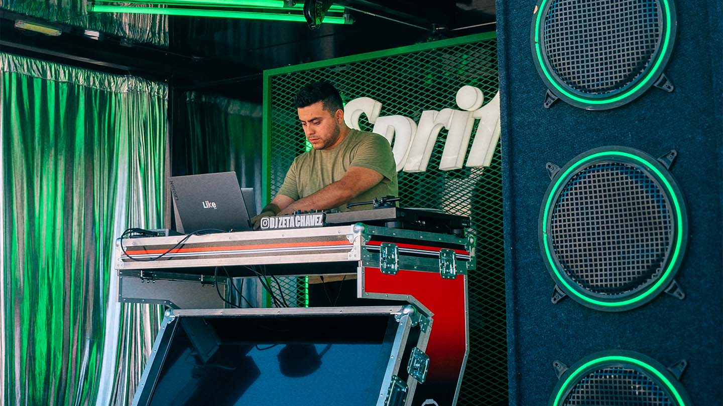 Dj tocando música en la consola en el concierto de Sprite RefresCAR con el logo de Sprite de fondo.