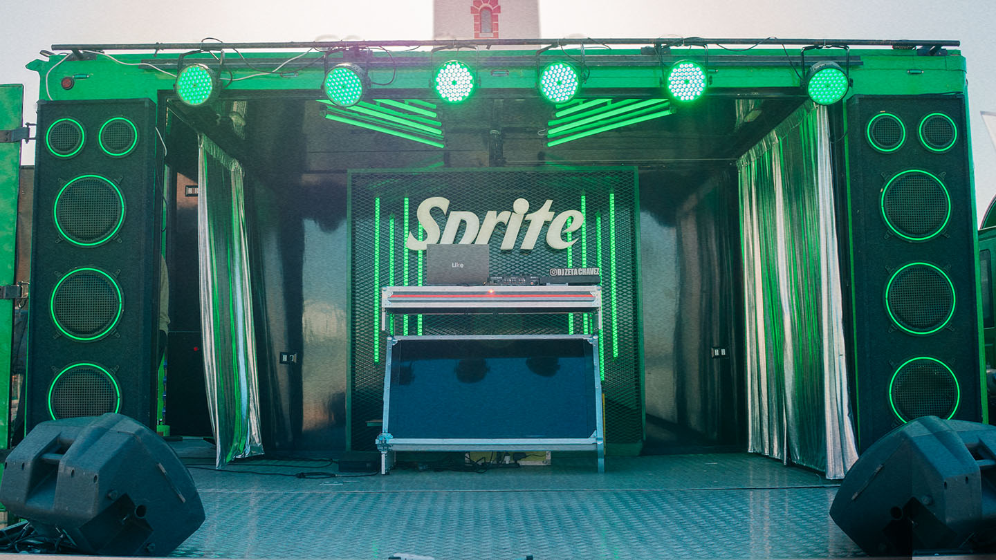 Escenario del Sprite RefresCAR iluminado con luces verdes, grandes parlantes a los costados y el logo de Sprite en el centro.