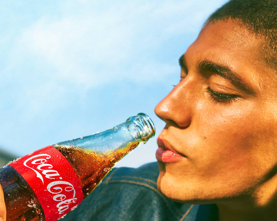 Hombre a punto de beber de una botella de Coca-Cola de vidrio en un día soleado.