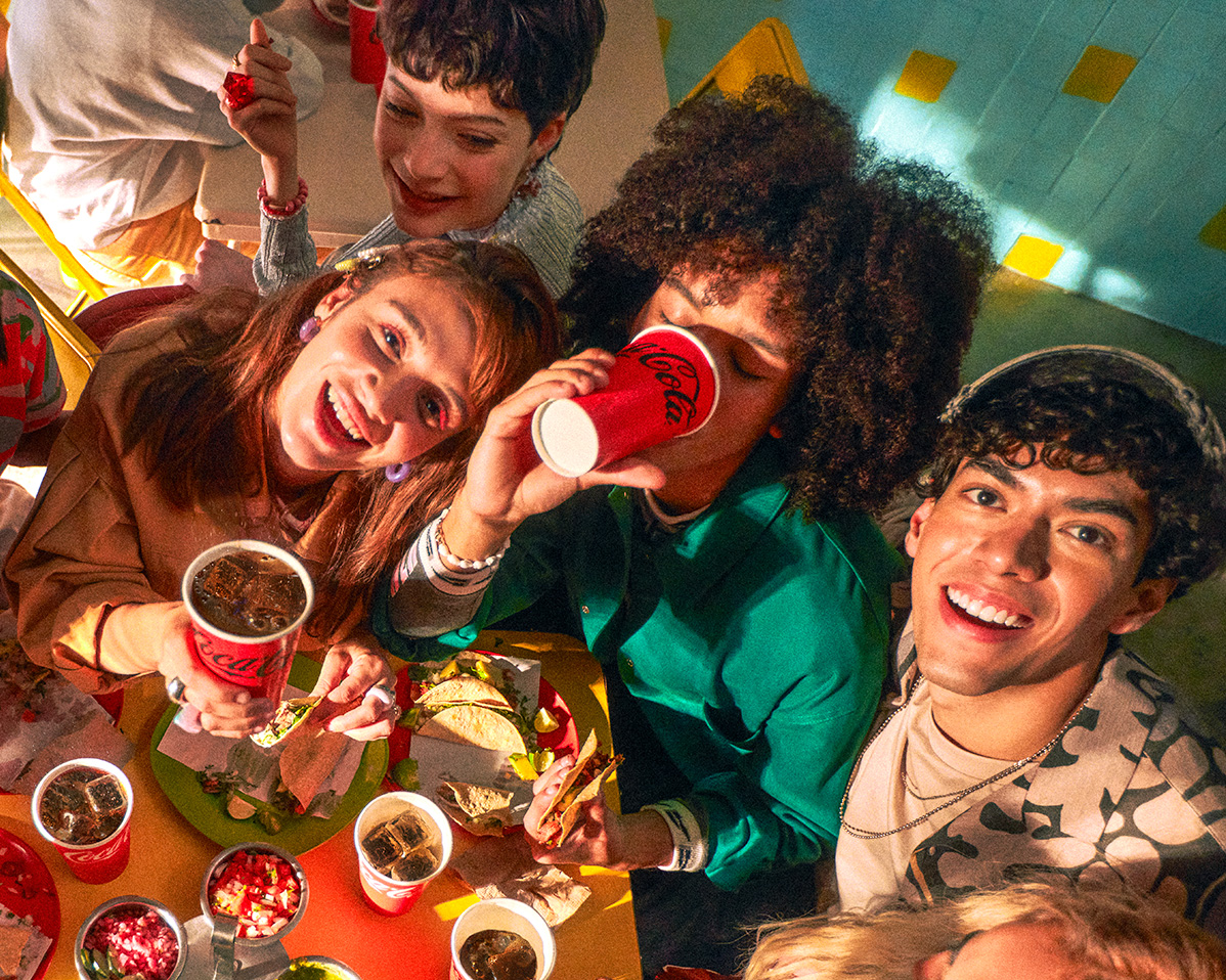 Grupo de amigos disfrutando de bebidas Coca-Cola en una fiesta, rodeados de comida.