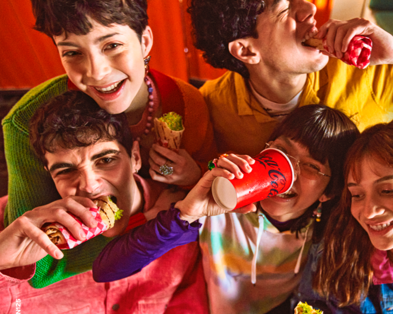 Grupo de amigos disfrutando de comida y bebidas Coca-Cola en una fiesta.