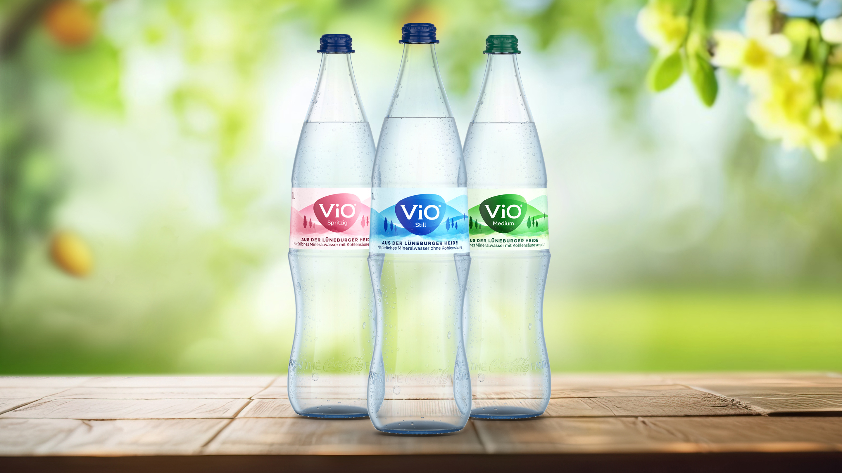 Drei verschiedene Flaschen ViO vor Hintergrund mit Wölkchen und Hügeln.