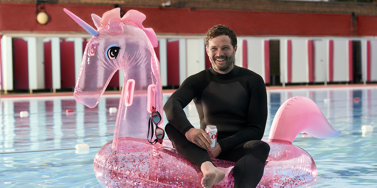 man sitting in a pool on an inflatable, holding a diet-coke