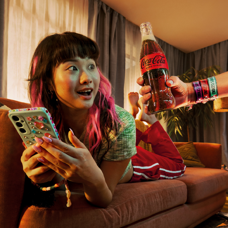 teen scrolling her phone enjoying a bottle of coca-cola zero sugar