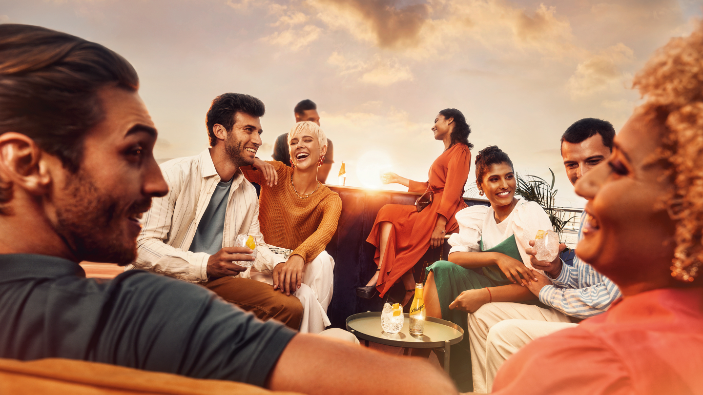 Group of friends sitting around a table outside enjoy Schweppes cocktails