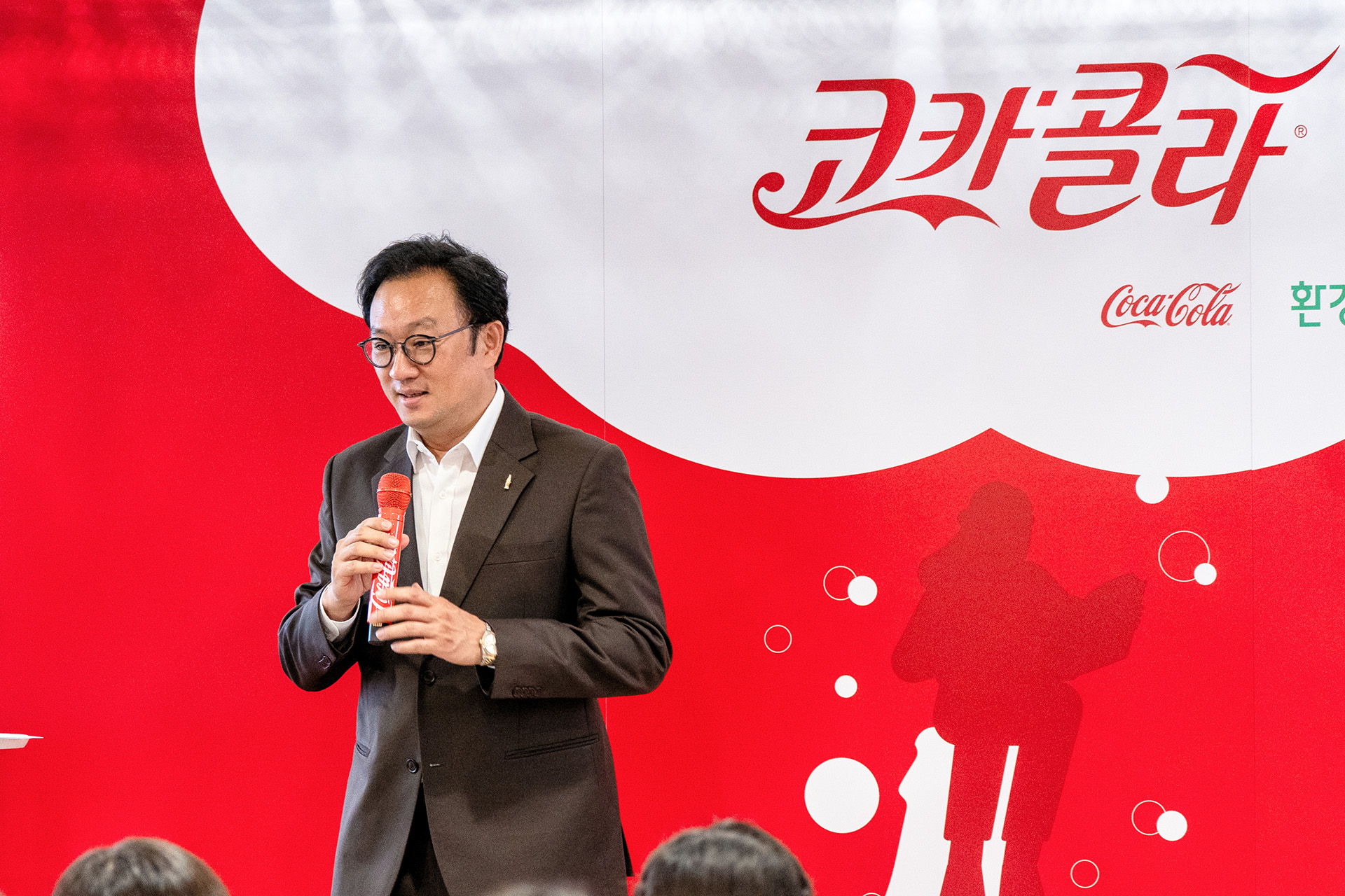 한국 코카콜라 정기성 대표가 코카콜라 로고가 새겨진 빨강색 마이크를 들고 장학생들에게 인삿말을 건네고 있다