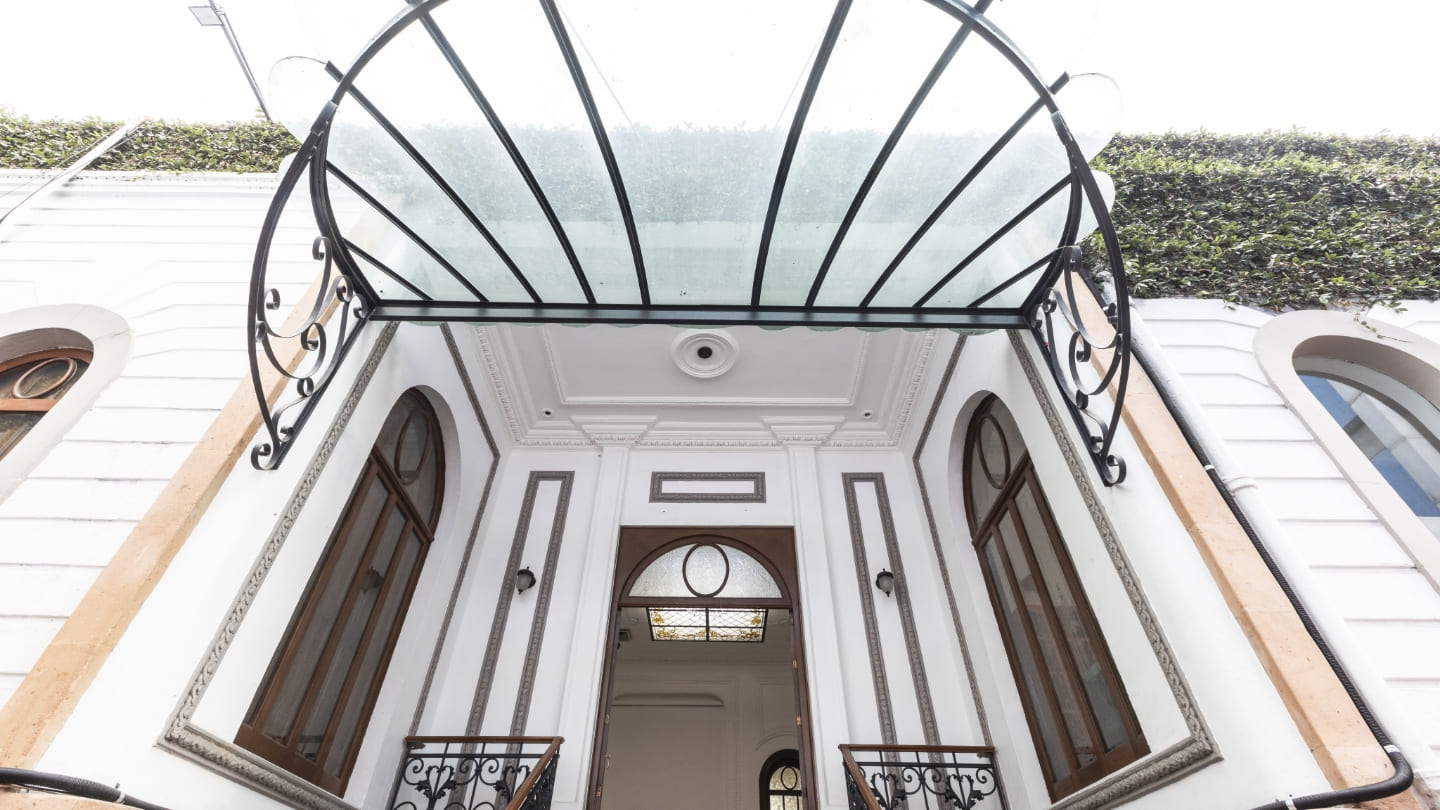 Entrada de una casa blanca con toldo de cristal y detalles ornamentales en México.