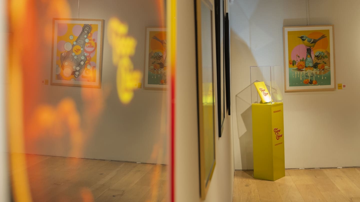 Interior de una galería con varias obras de arte con temática de Topo Chico en las paredes y un pedestal.