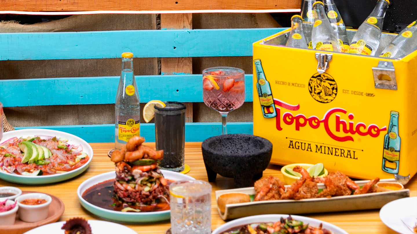 Mesa con distintos platos de comida y botellas de Topo Chico Agua.