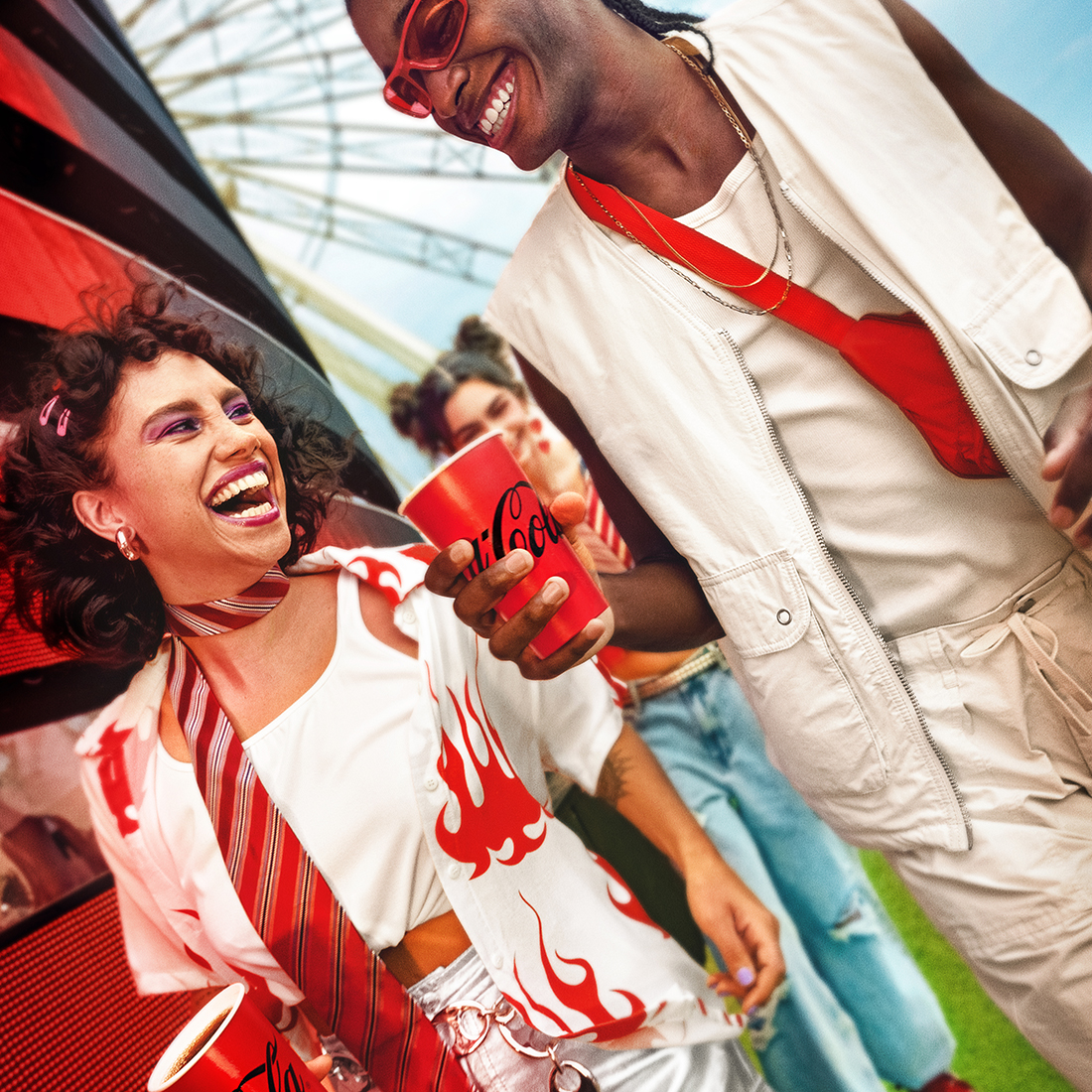  Dos personas disfrutando de una Coca-Cola, sonriendo y riendo. Una persona tiene el pelo rizado con accesorios rosados y lleva una bufanda a rayas, mientras que la otra persona tiene trenzas, usa gafas de sol, un chaleco blanco y una bolsa cruzada roja. Líneas gráficas rojas mejoran el ambiente festivo.​