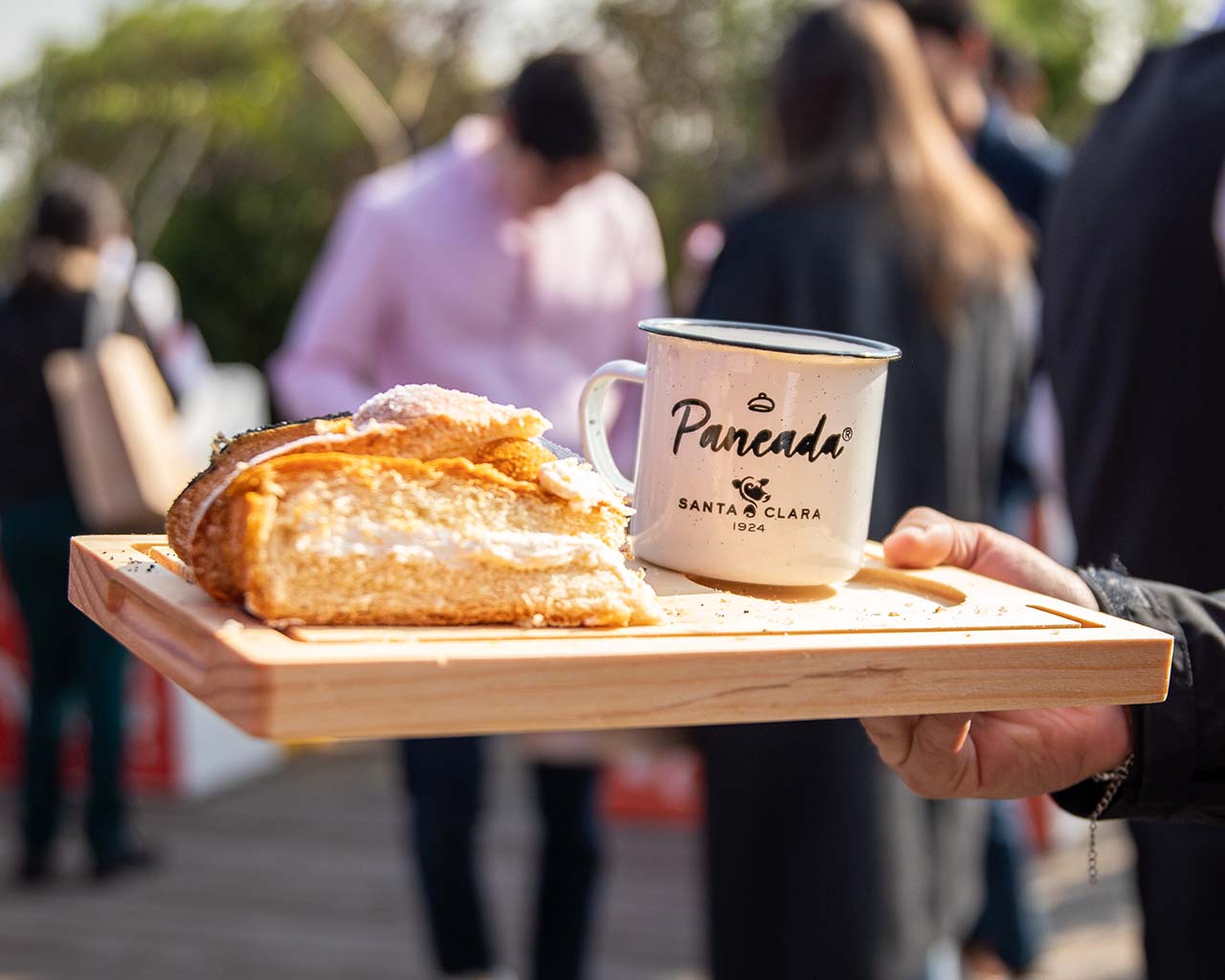 imagen de una persona sosteniendo una tabla con una taza con el texto: Paneada, Santa Clara. En la tabla también hay diferentes preparaciones dulces 