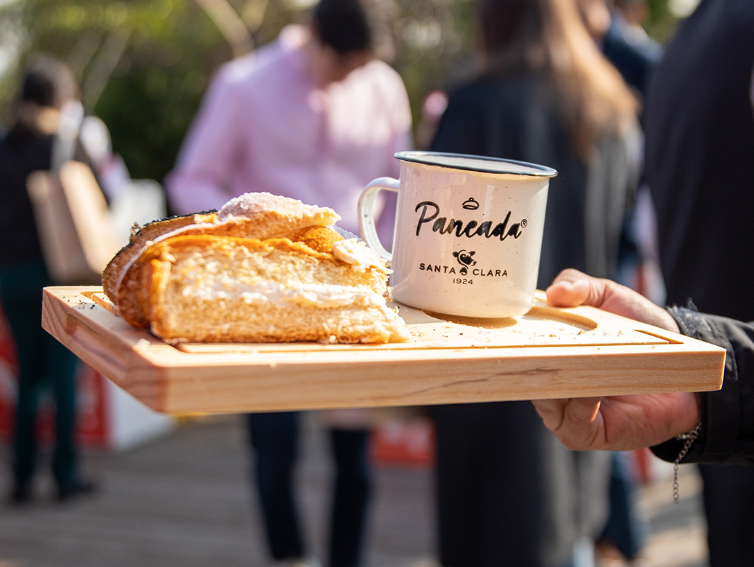 Persona sosteniendo una bandeja de madera con una preparación dulce y una taza con el logo Santa Clara