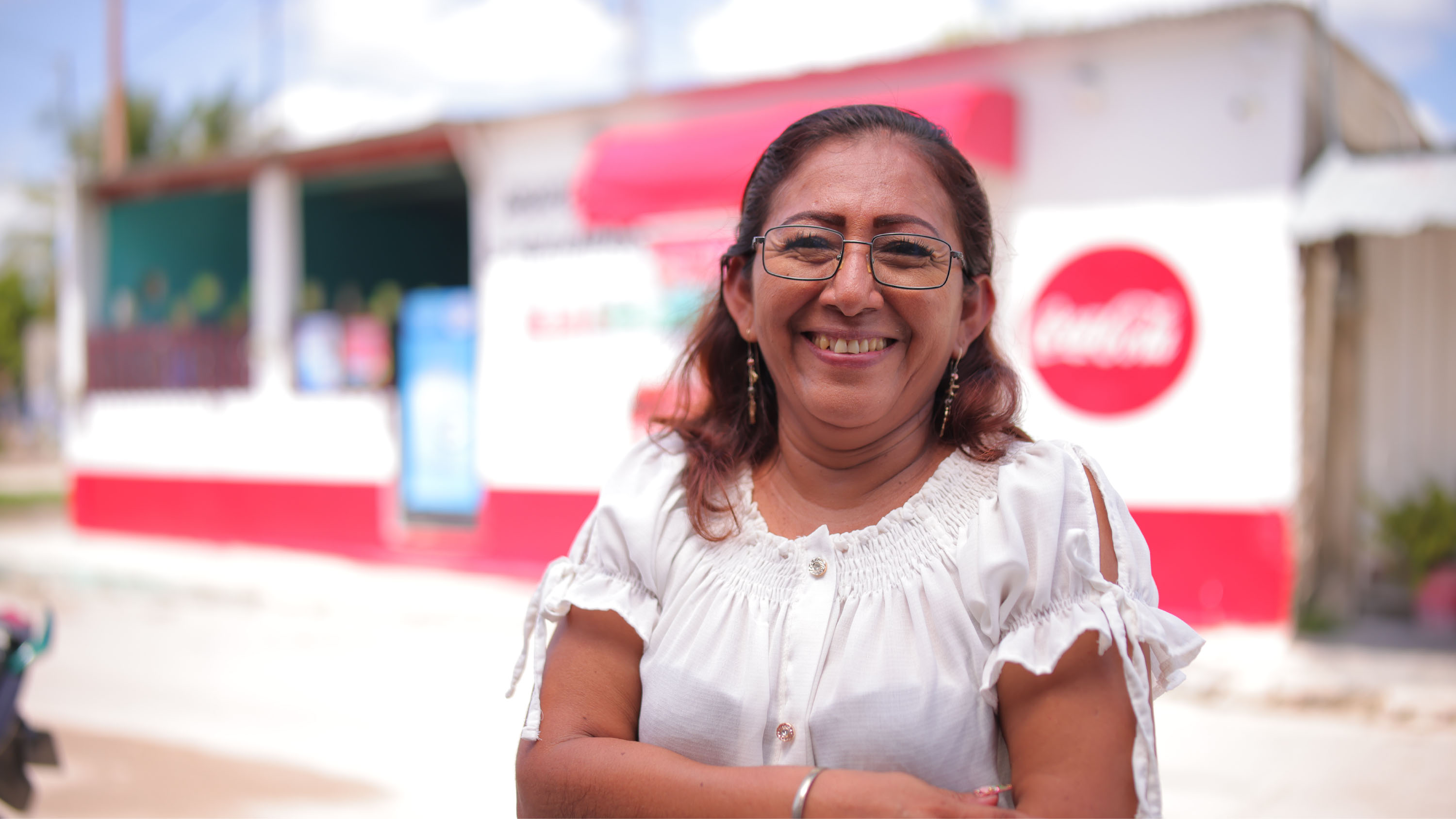 Mujer mirando a cámara sonriente. De fondo se observa un almacén con el logo de Coca-Cola en su fachada.