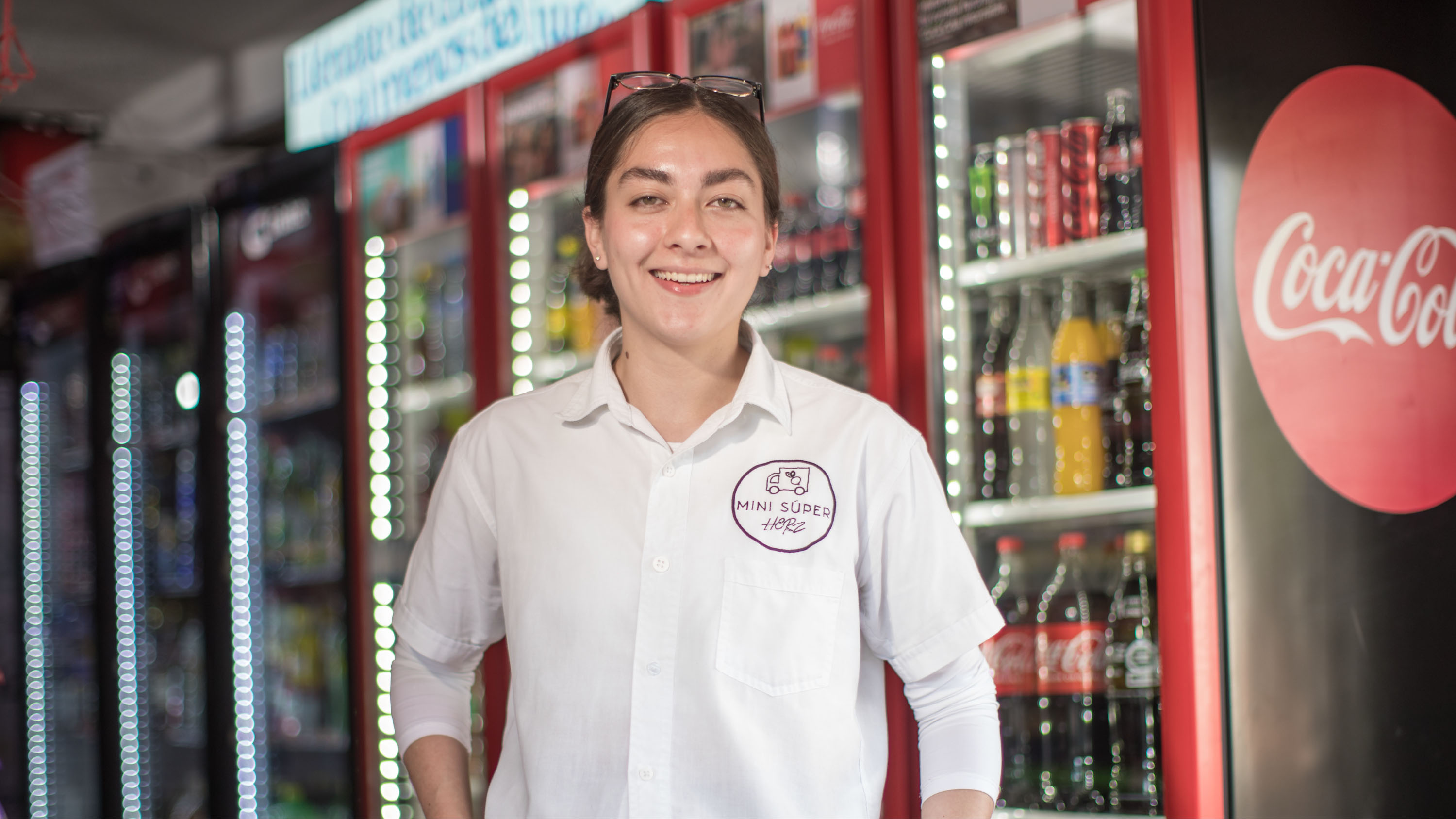 Mujer mirando a cámara sonriente. De fondo se observan heladeras con productos Coca-Cola en su interior.