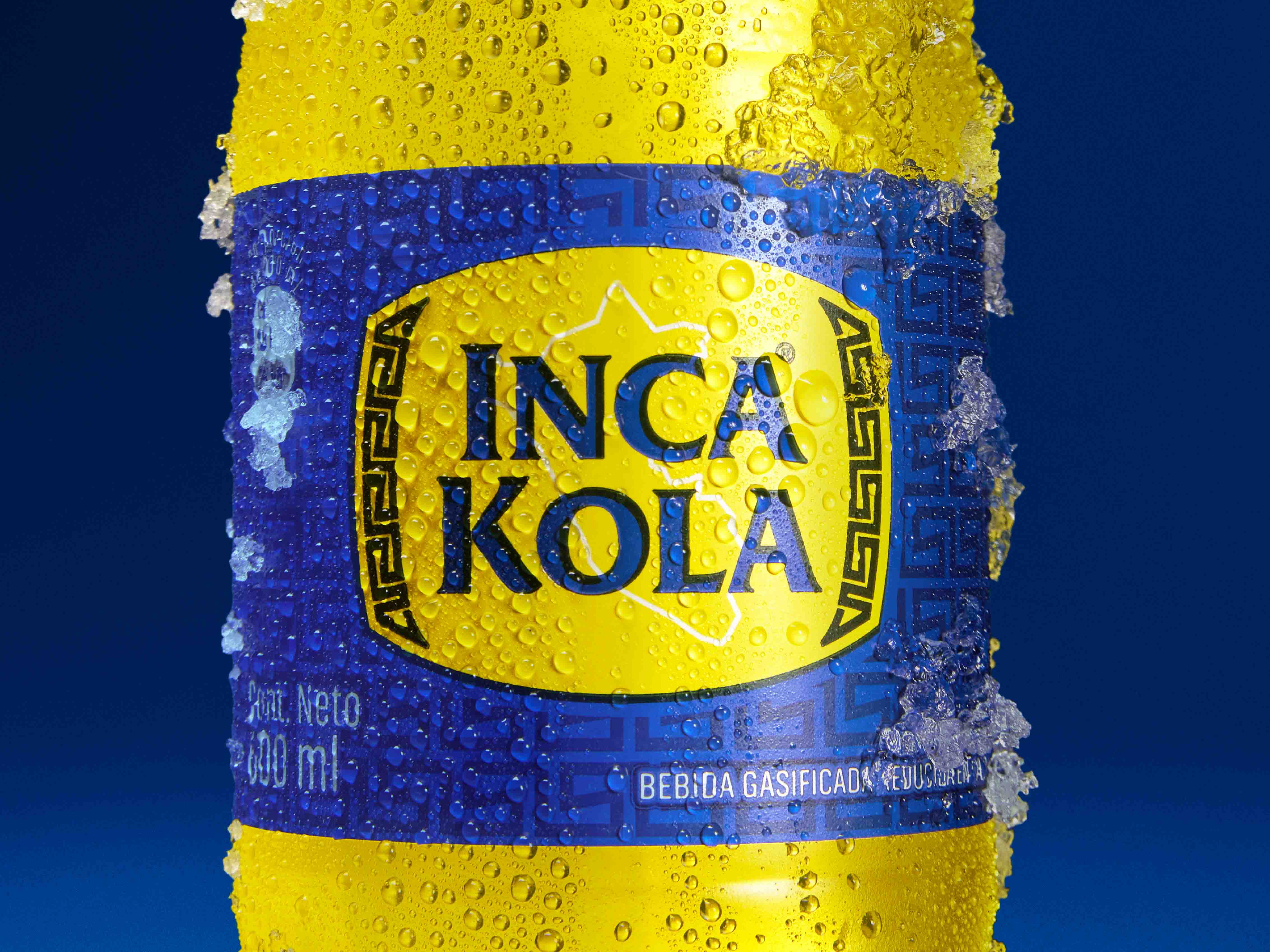 Primer plano de una botella de Inca Kola fría sobre un fondo azul.