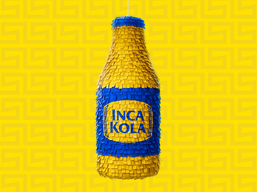 Piñata con forma de botella de Inca Kola sobre un fondo amarillo.