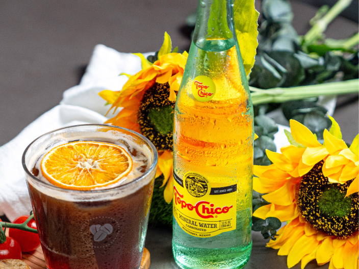 Sparkling blood orange espresso topped with orange slice and next to a bottle of Topo Chico