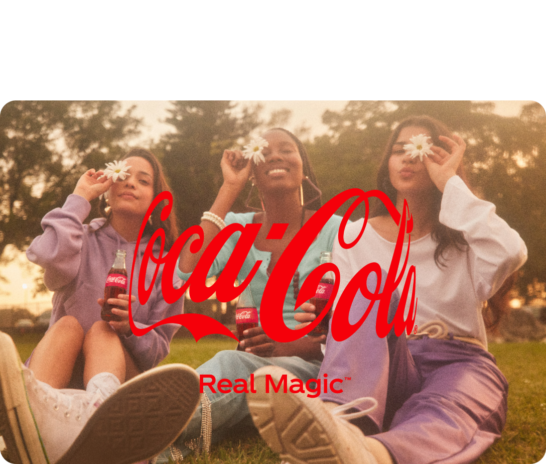 Coca Cola logo in the foreground with 3 girls in the back ground sitting down holding coca cola's and flowers