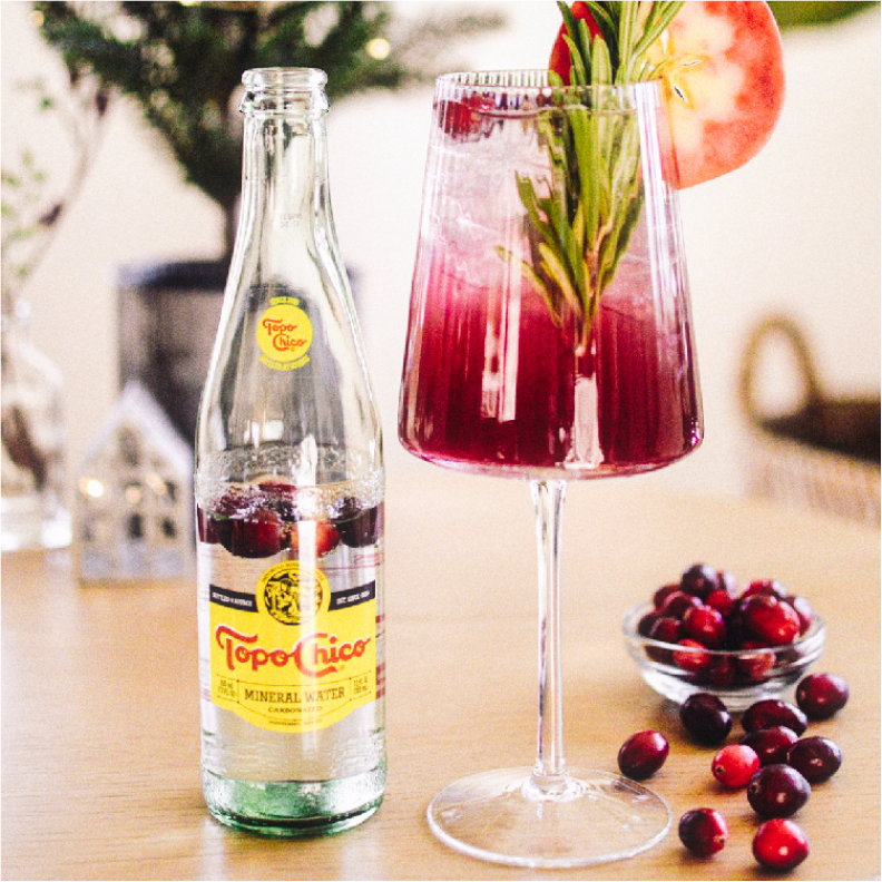 threes bottles of Topo Chico next to a glass with the Rosemary Ginger Spritz drink