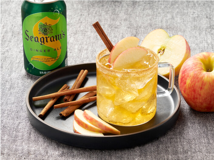 an amber apple drink with cloves and apple slices beside a seagram's drink