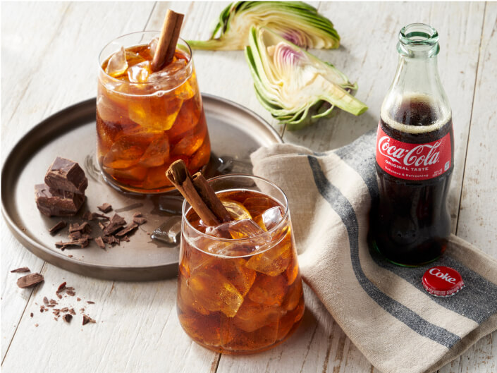 two cola colored drinks next to a coke